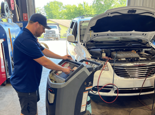 Technician performing AC system diagnostics with gauges and scan tool